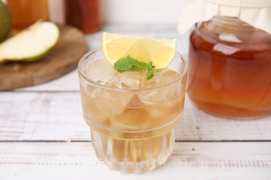 Tasty kombucha and ice cubes in glass on white wooden table, closeup