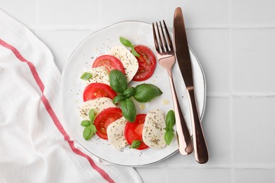 Photo of Caprese salad with tomatoes, mozzarella, basil and spices served on white tiled table, flat lay