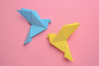 Beautiful colorful origami birds on pink background, flat lay