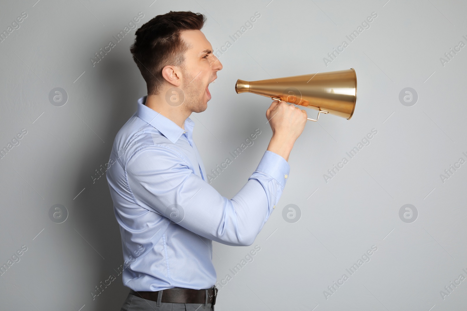 Photo of Young man shouting into megaphone on light background
