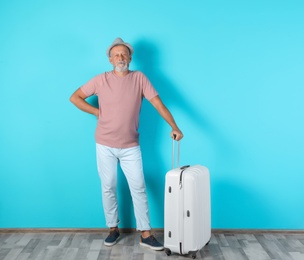 Senior man with suitcase near color wall. Vacation travel