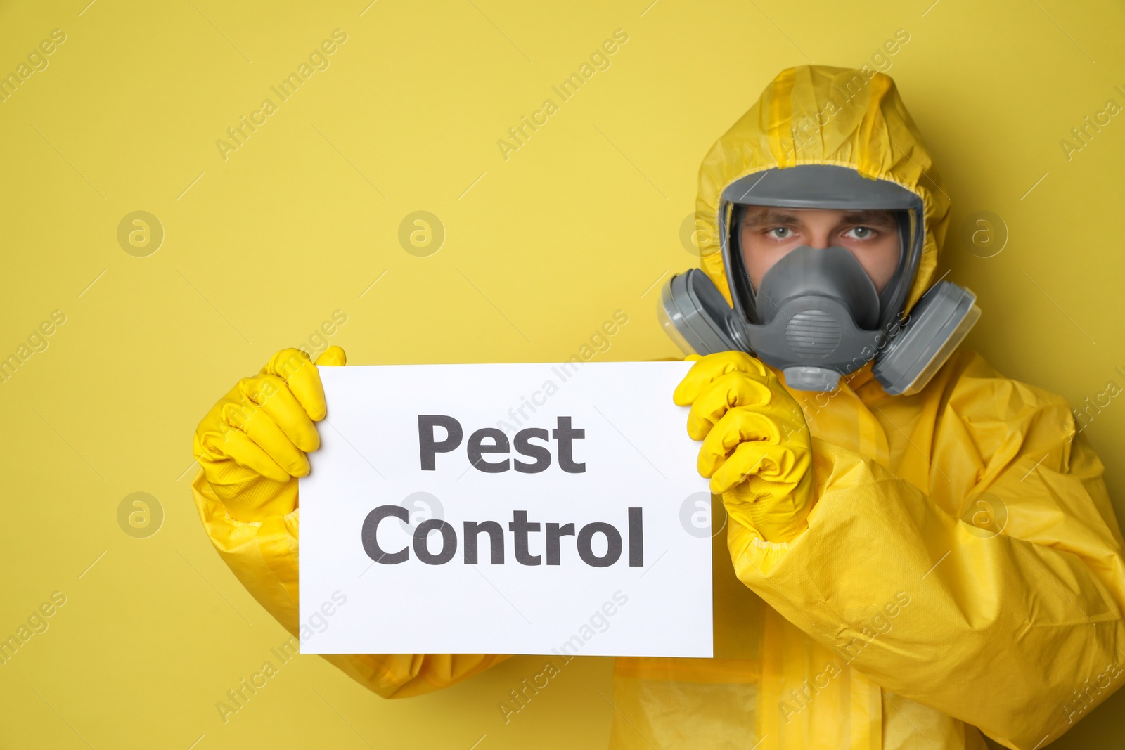 Photo of Man wearing protective suit with insecticide sprayer holding sign PEST CONTROL on yellow background