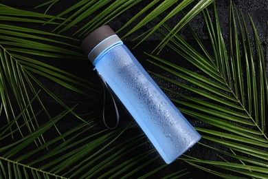 Wet thermo bottle and green leaves on black table, top view