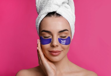 Photo of Beautiful young woman with under eye patches and hair wrapped in towel on pink background