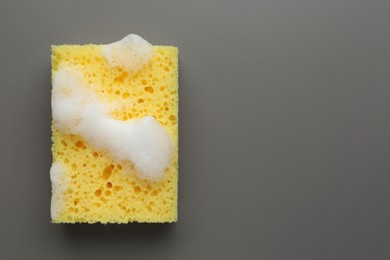 Photo of Yellow sponge with foam on grey background, top view. Space for text