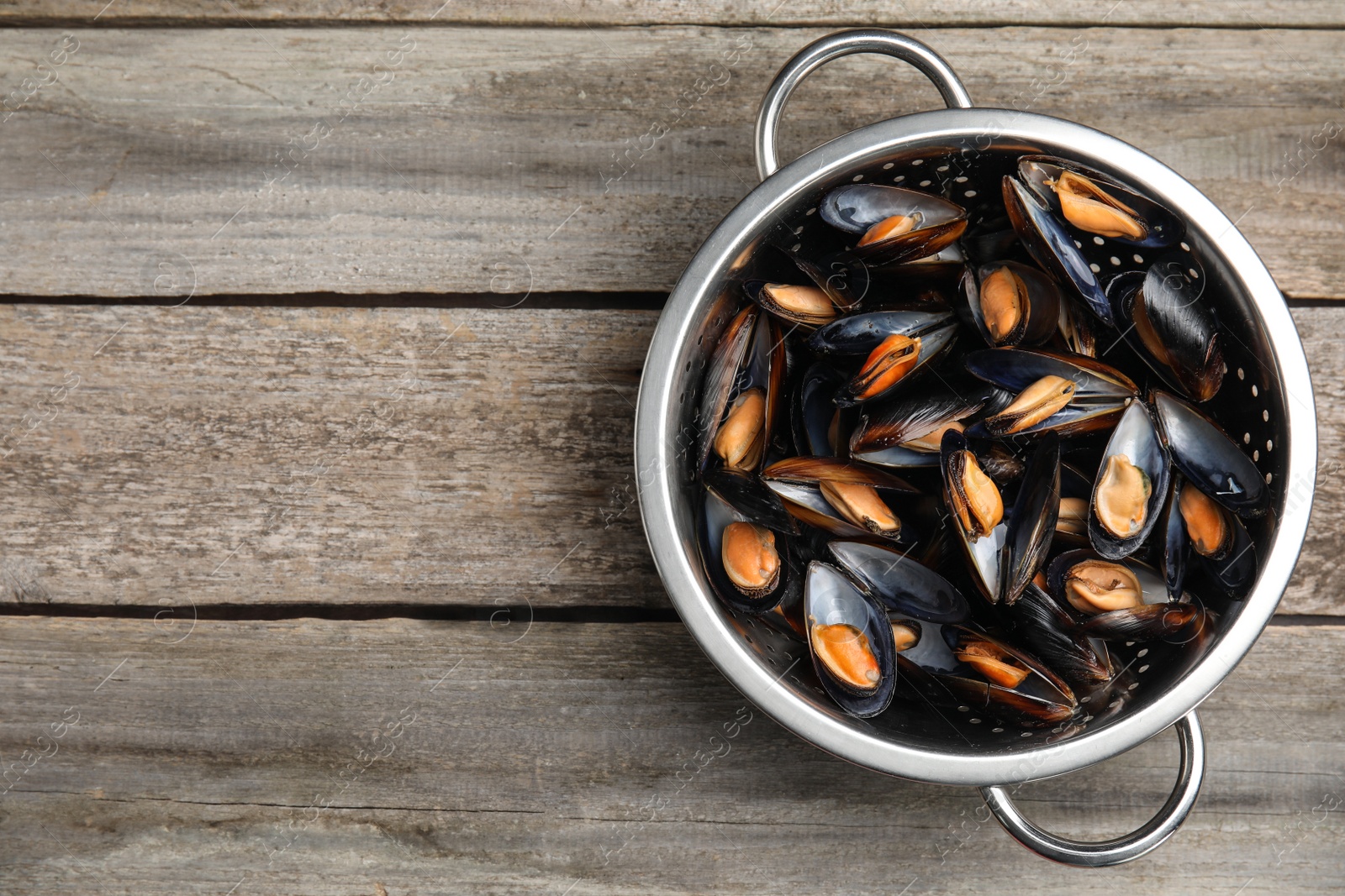 Photo of Colander with delicious cooked mussels on wooden table, top view. Space for text