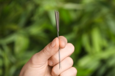 Woman holding needles for acupuncture on blurred green background, closeup