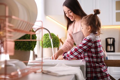 Photo of Mother and daughter washing dishes together in kitchen at home