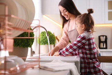 Mother and daughter washing dishes together in kitchen at home