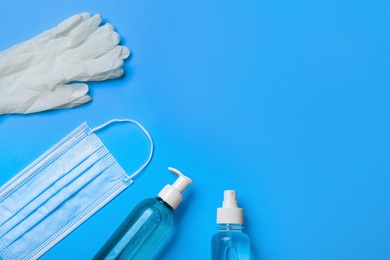 Photo of Medical gloves, mask and hand sanitizers on light blue background, flat lay. Space for text