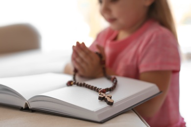 Photo of Cute little girl with beads praying over Bible at home. Space for text