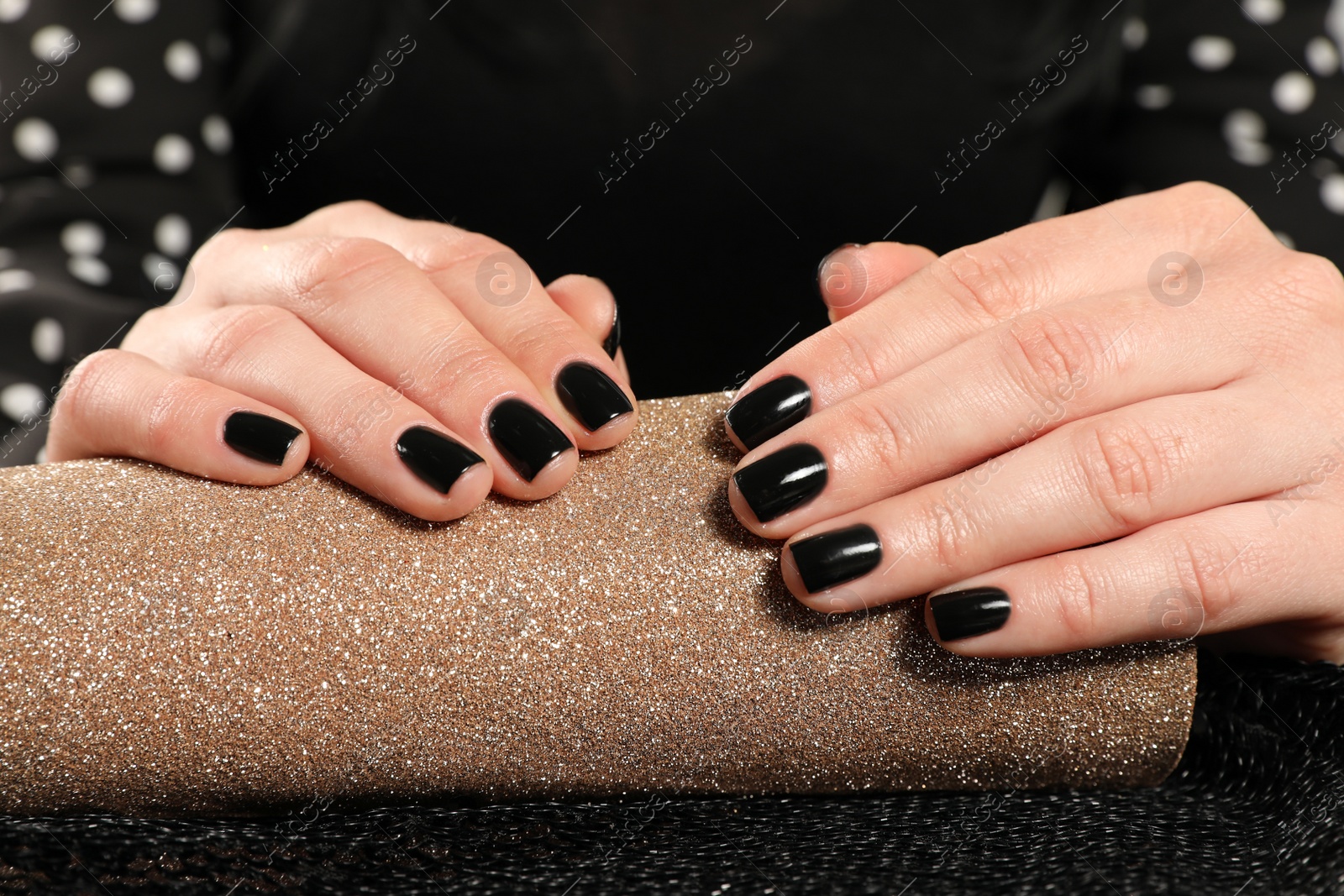 Photo of Woman showing black manicure on rolled shiny paper, closeup. Nail polish trends