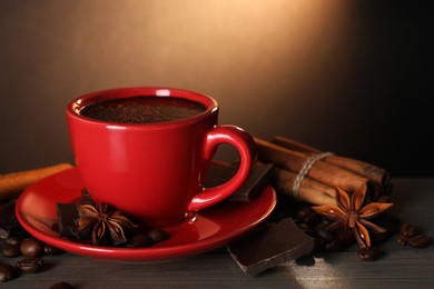 Photo of Cup of delicious hot chocolate, spices and coffee beans on wooden table