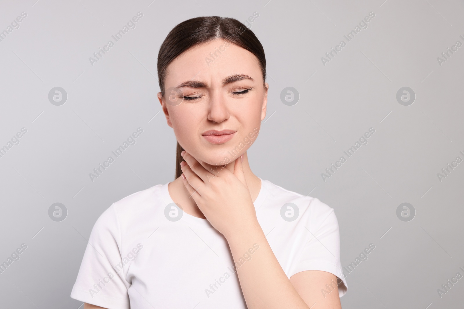 Photo of Young woman with sore throat on light grey background