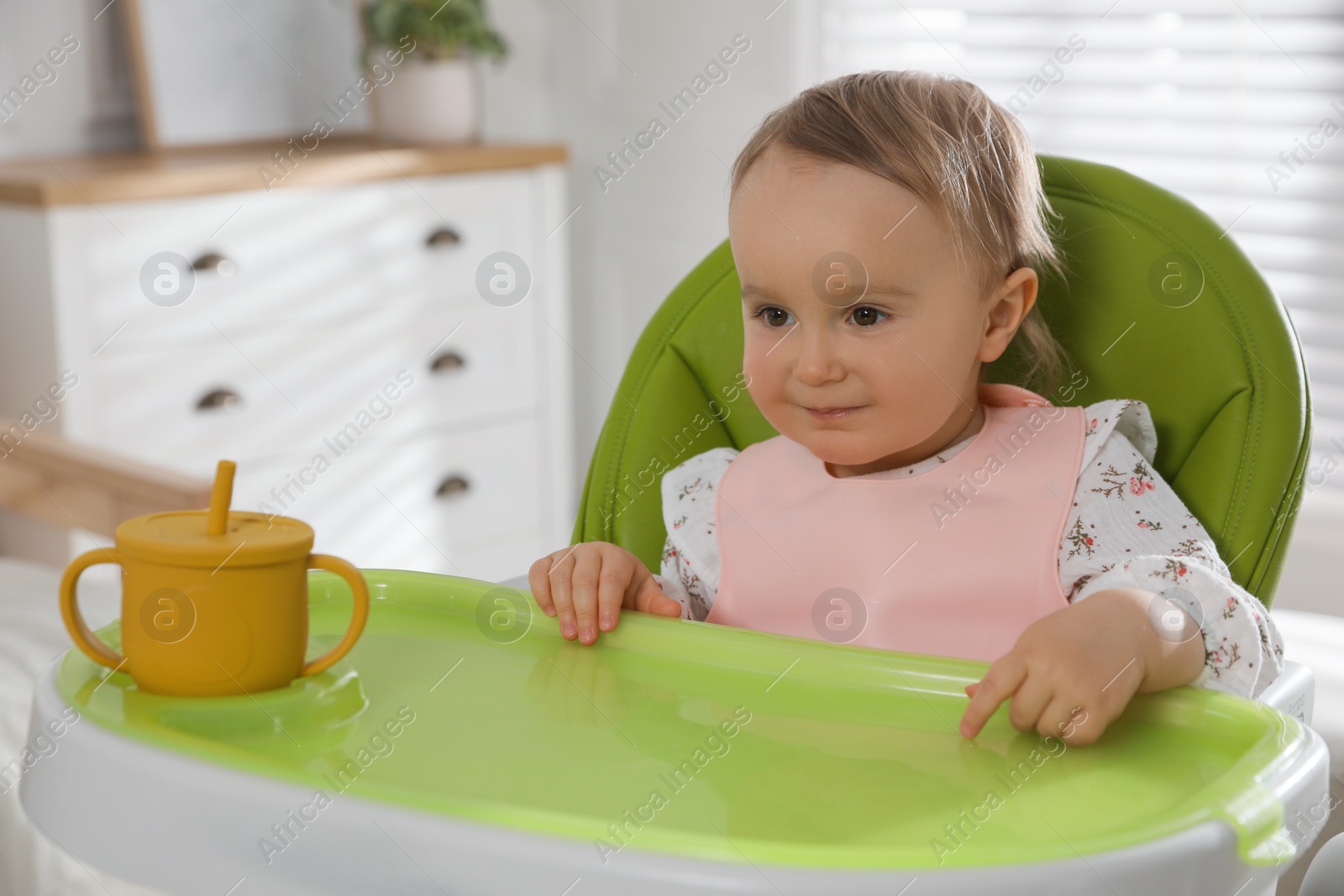 Photo of Cute little baby wearing bib in highchair at home