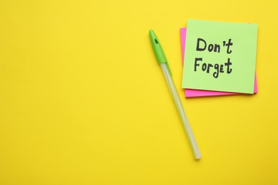 Photo of Paper note with phrase Don' t Forget and pen on yellow background, flat lay. Space for text