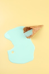 Melted ice cream and wafer cone on beige background, top view