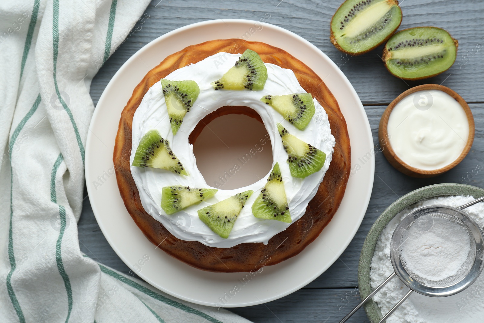 Photo of Homemade yogurt cake with kiwi and cream on grey wooden table, flat lay
