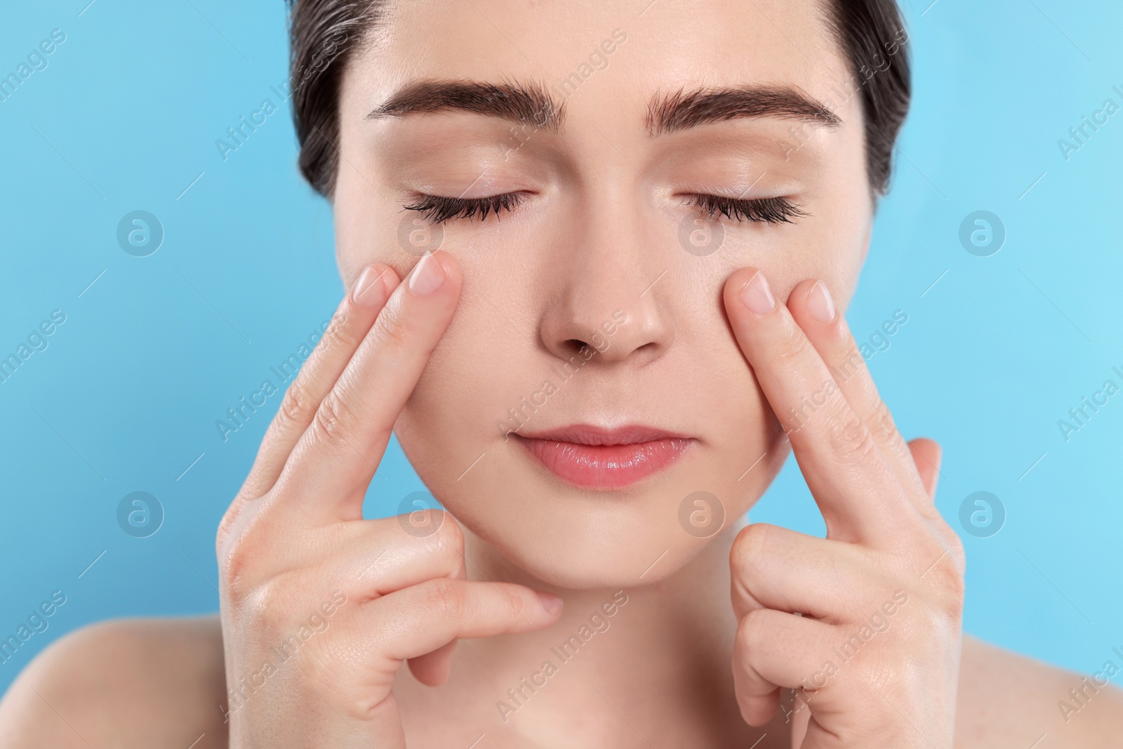 Photo of Young woman massaging her face on turquoise background