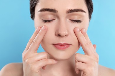 Young woman massaging her face on turquoise background