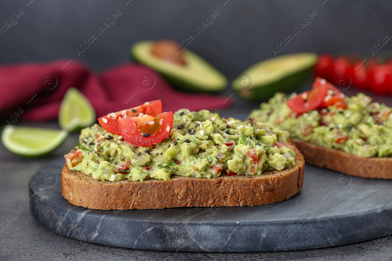 Photo of Slices of bread with tasty guacamole and ingredients on grey table, closeup
