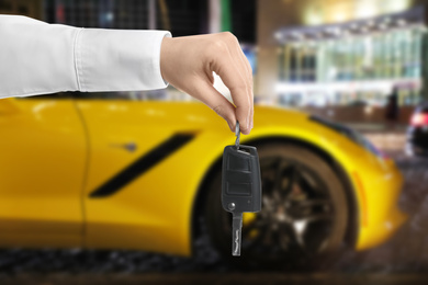 Car buying. Man holding key against blurred automobile, closeup
