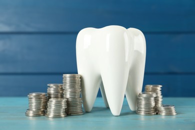 Photo of Ceramic model of tooth and coins on light blue wooden table. Expensive treatment
