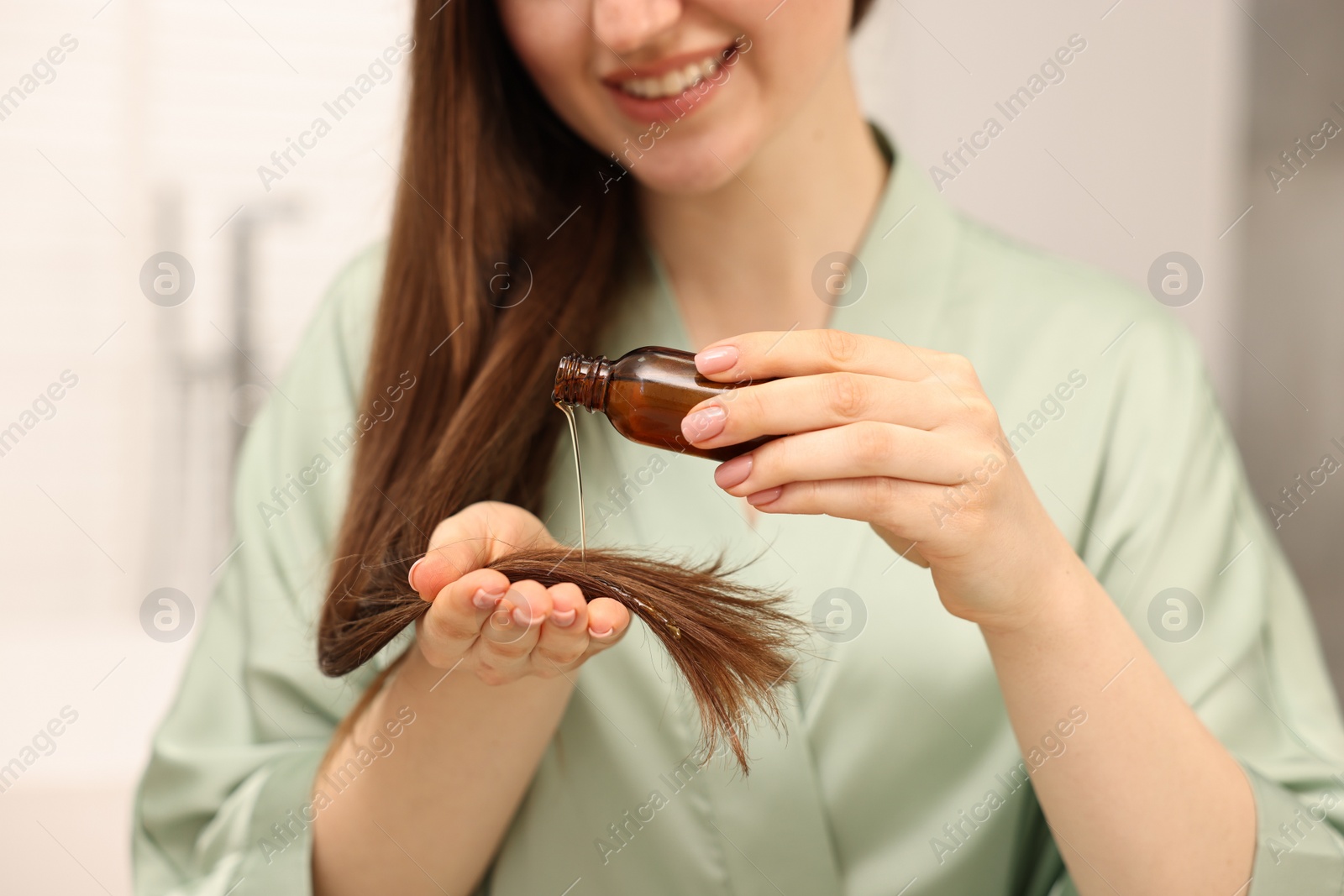 Photo of Woman applying oil hair mask indoors, closeup