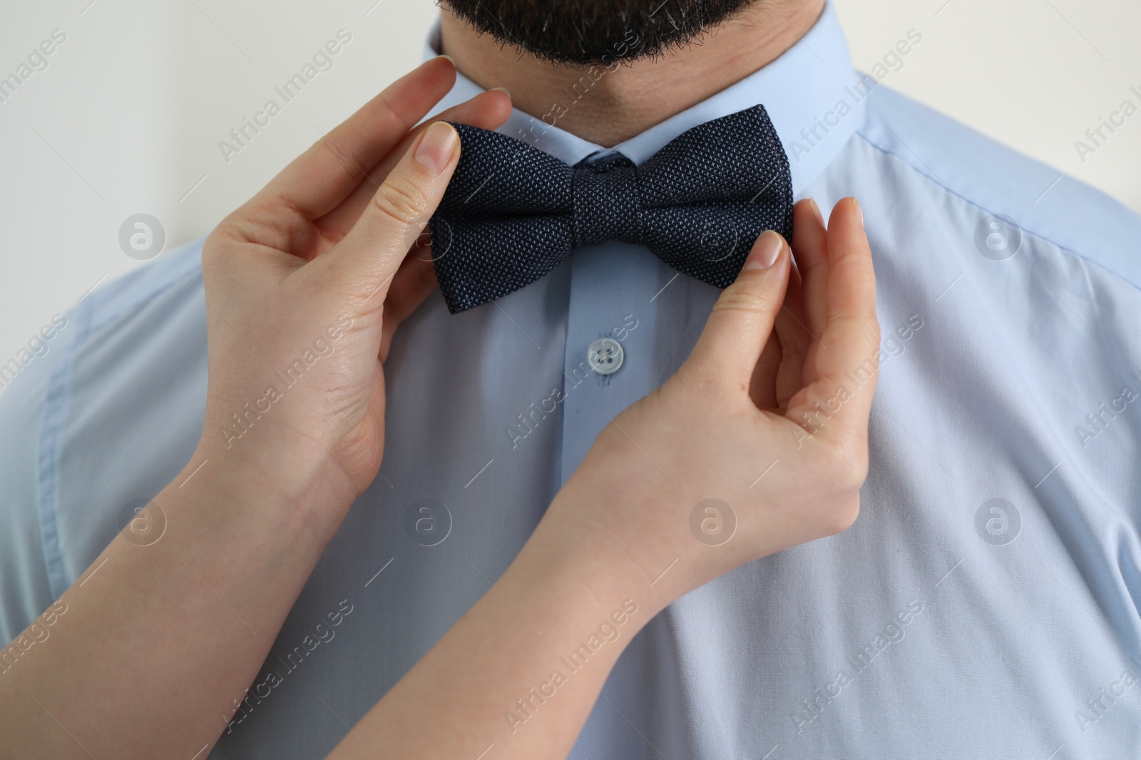 Photo of Woman adjusting bow tie to man indoors, closeup