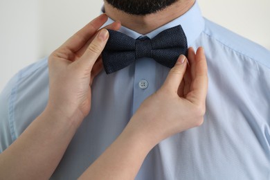 Photo of Woman adjusting bow tie to man indoors, closeup