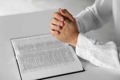 Photo of Man with Bible praying at white table indoors, closeup