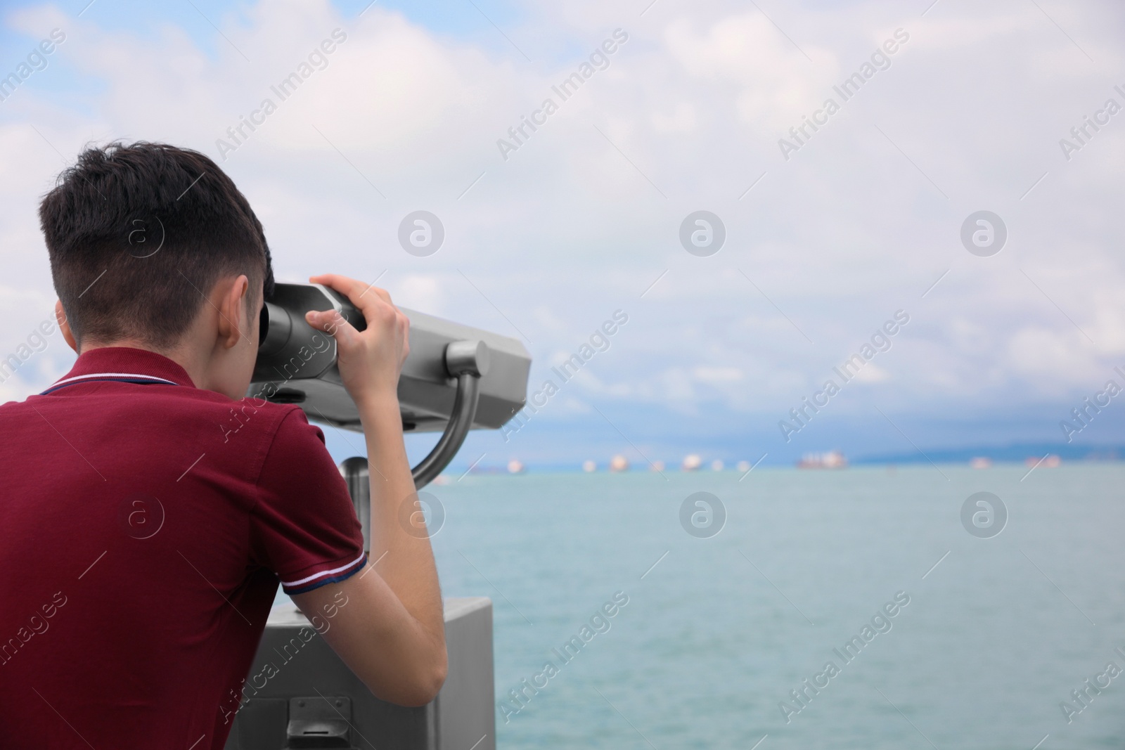 Photo of Teenage boy looking through mounted binoculars at mountains. Space for text