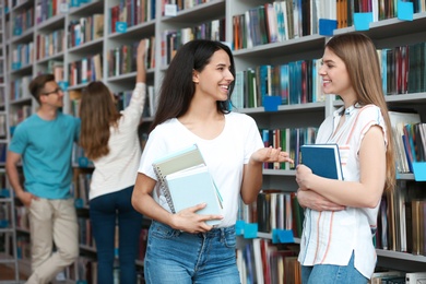Photo of Young people standing near bookshelves in library