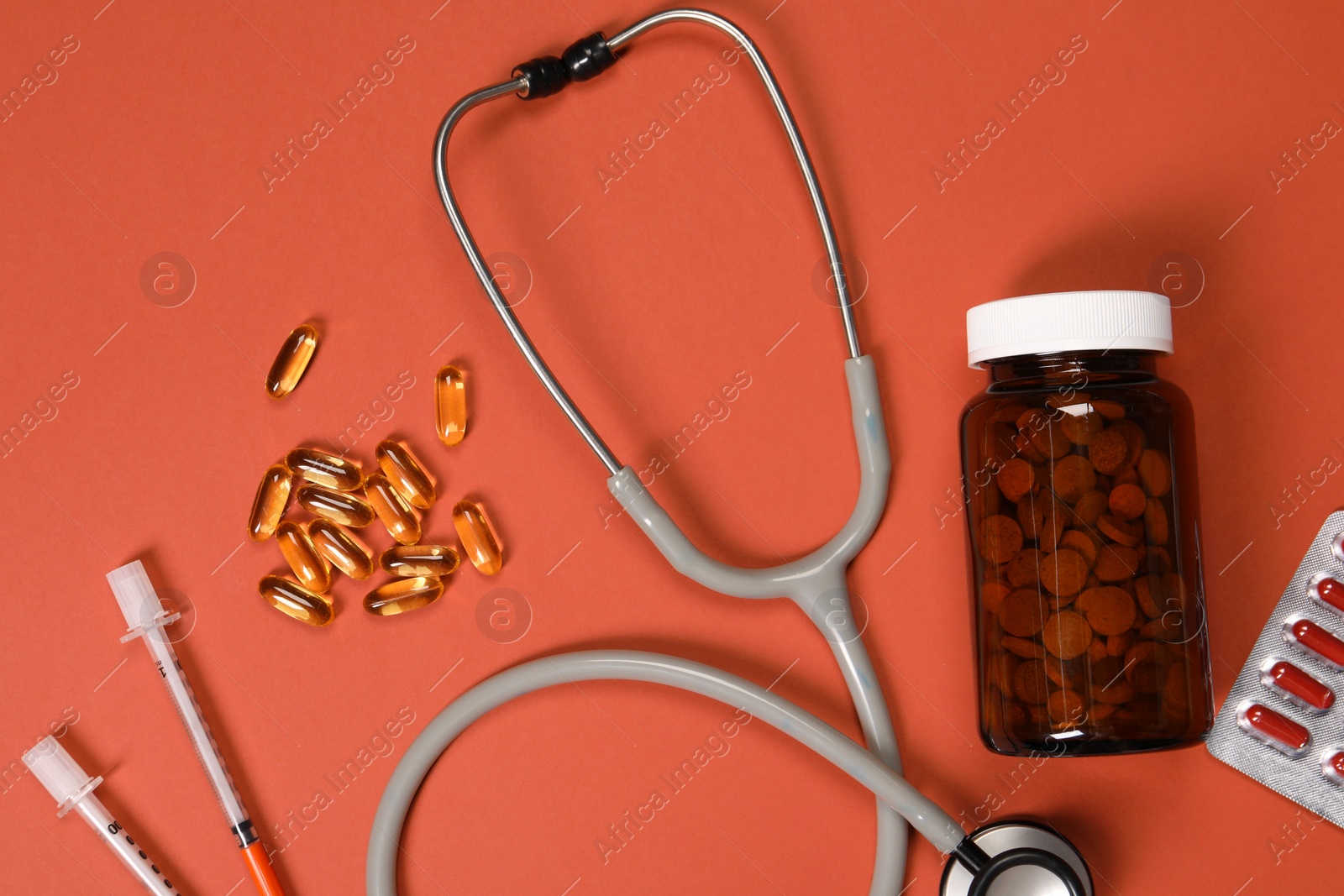 Photo of Stethoscope, syringes and pills on crimson background, flat lay. Medical tools