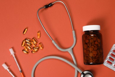 Photo of Stethoscope, syringes and pills on crimson background, flat lay. Medical tools