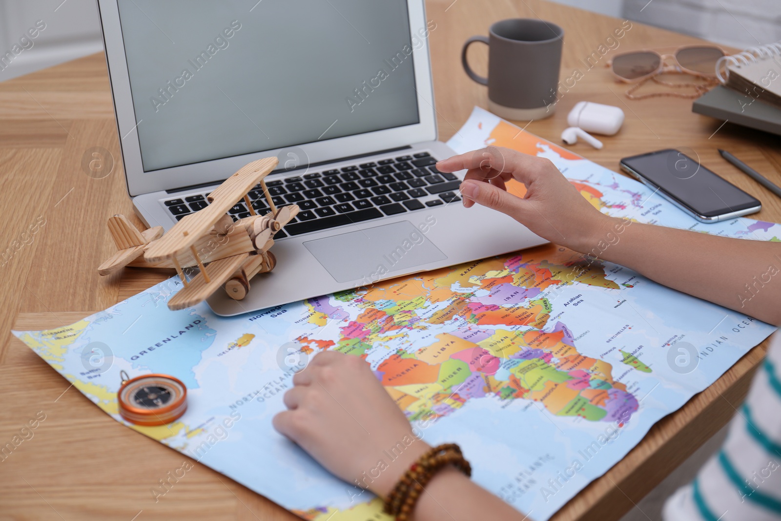 Photo of Woman with world map and laptop planning trip at wooden table, closeup