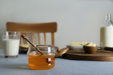 Photo of Jar with honey, milk and butter served for breakfast on grey table