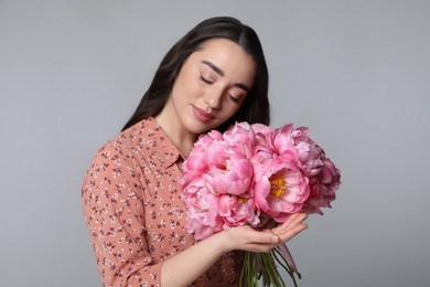 Beautiful young woman with bouquet of peonies on light grey background