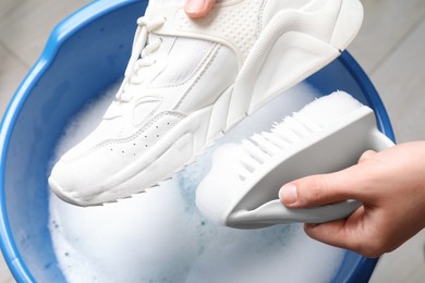 Photo of Woman cleaning stylish sneakers with brush in wash basin, top view