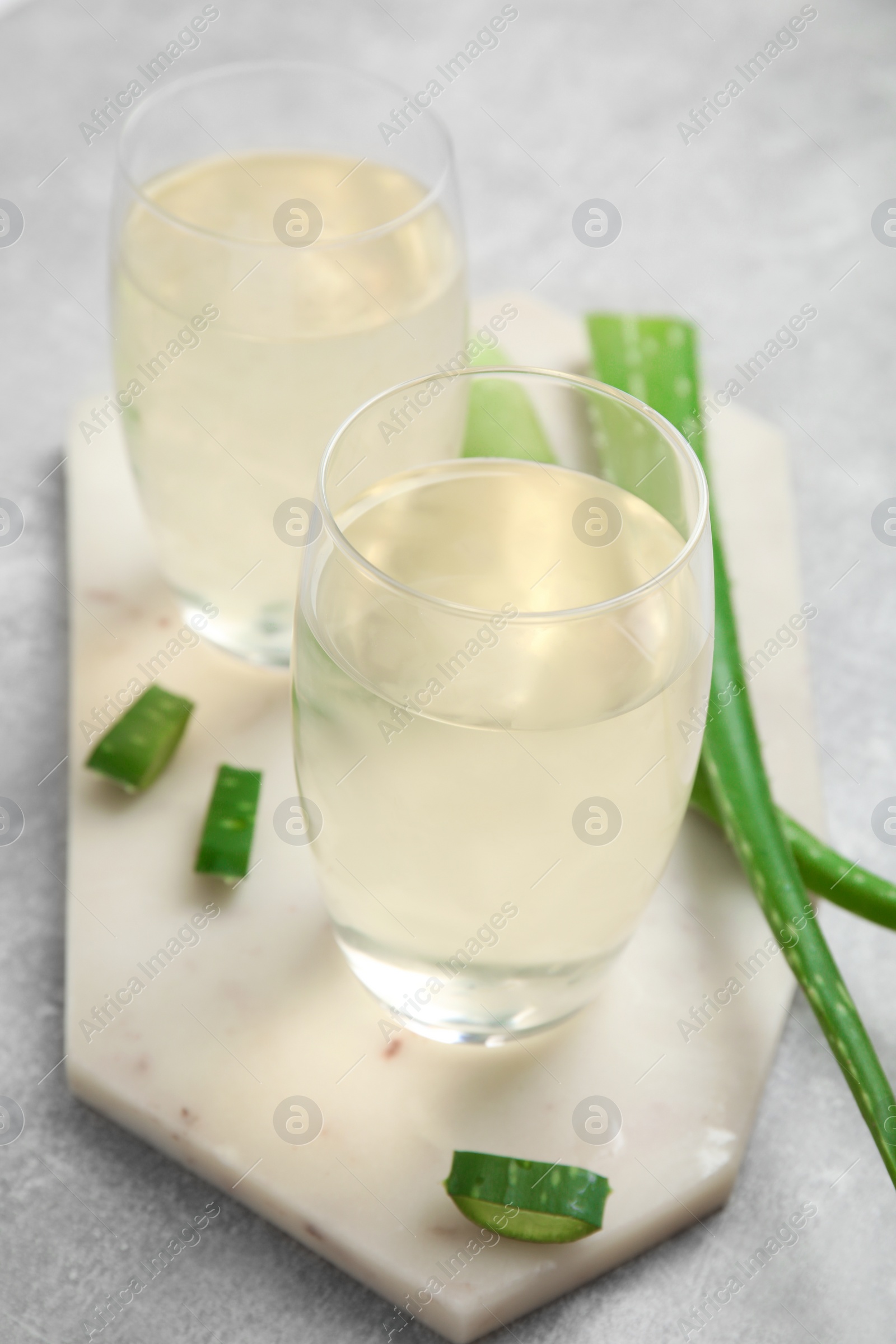 Photo of Fresh aloe drink in glasses and leaves on light grey table