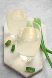 Photo of Fresh aloe drink in glasses and leaves on light grey table