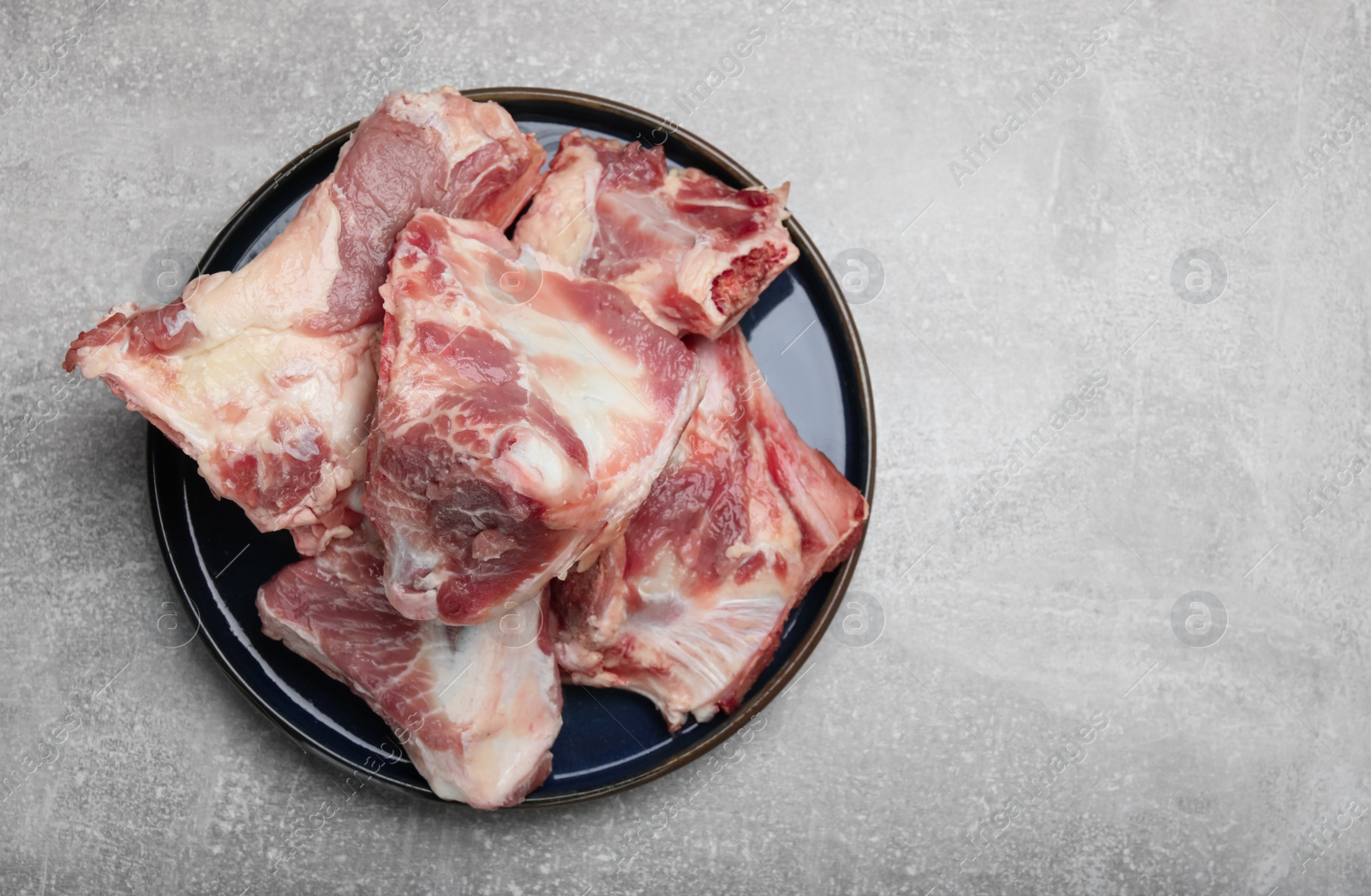 Photo of Plate with raw chopped meaty bones on grey table, top view. Space for text