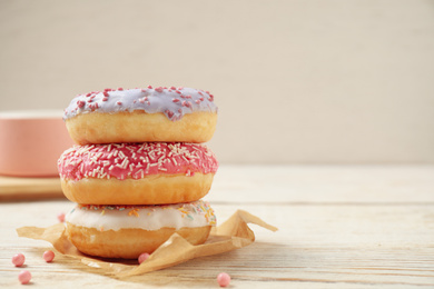 Photo of Delicious glazed donuts on white wooden table. Space for text