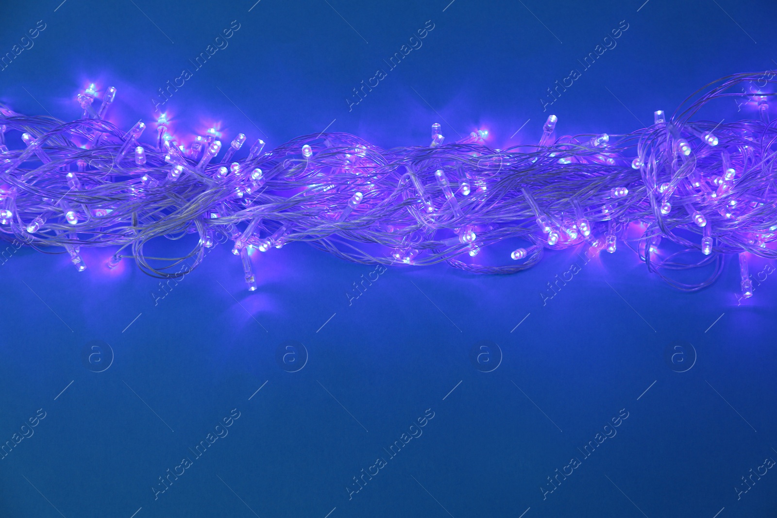 Photo of Glowing Christmas lights on dark blue background, space for text