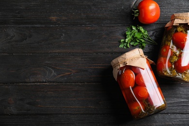 Flat lay composition with pickled tomatoes in glass jars on black wooden table, space for text