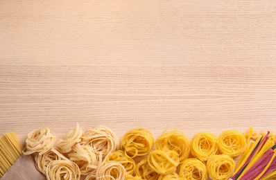 Different types of pasta on wooden table, flat lay. Space for text