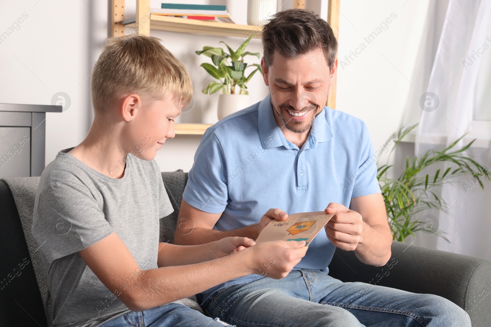 Photo of Happy man receiving greeting card from his son at home