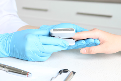 Photo of Doctor examining patient with fingertip pulse oximeter at white wooden table in office, closeup