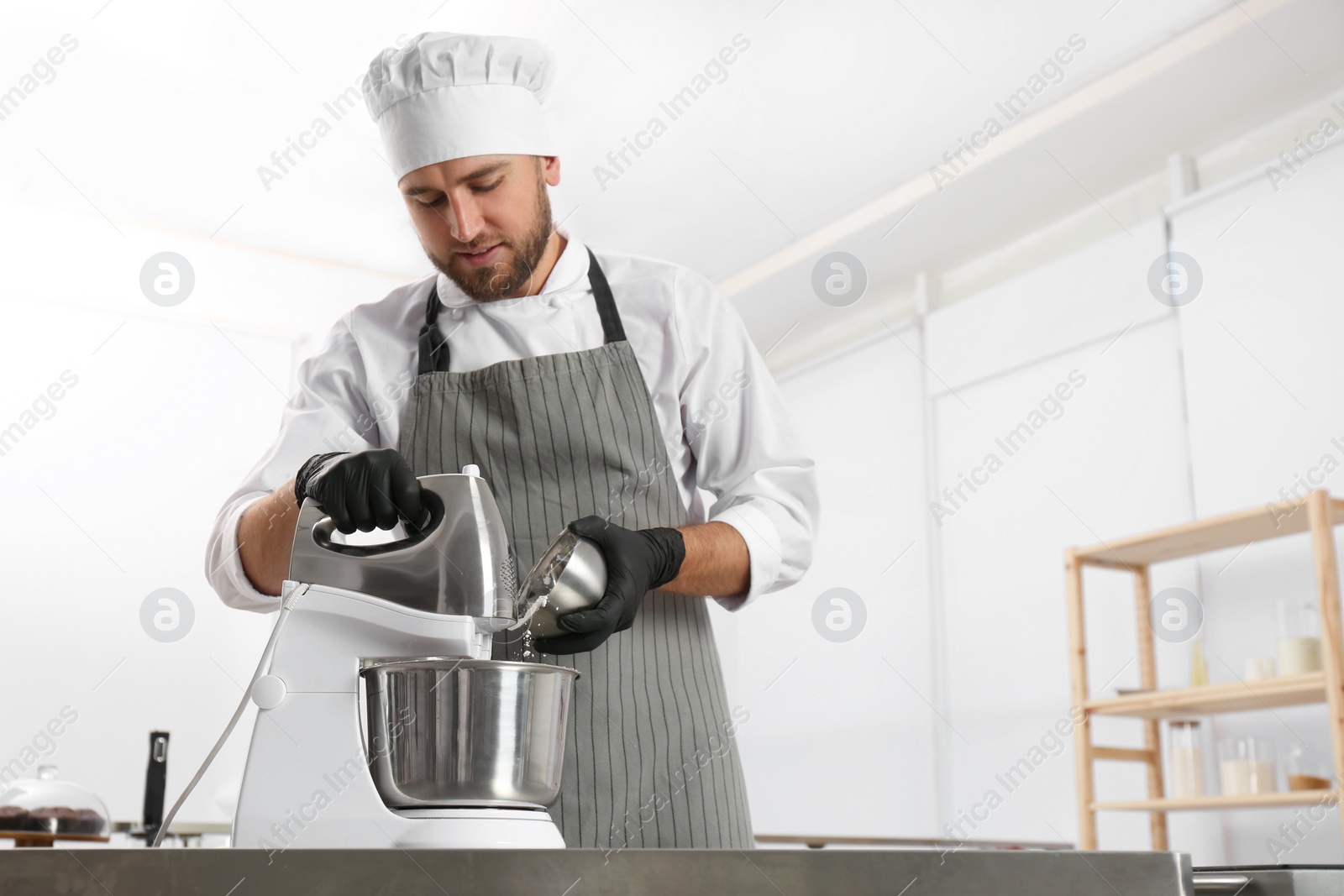Photo of Male pastry chef preparing dough in mixer at kitchen table