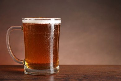 Photo of Mug with fresh beer on wooden table against brown background. Space for text